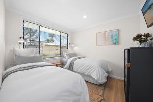 a white bedroom with two beds and a window at Little Palm Cabins in Lake Cathie