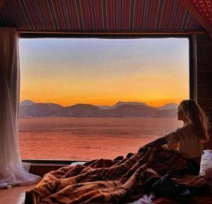 uma mulher deitada na cama olhando para fora de uma janela em moon city with jeep trips em Wadi Rum