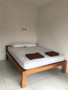 uma cama com lençóis brancos e almofadas castanhas em Makini Guest House em Lambangkuning