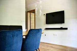 mesa con 2 sillas azules y TV en la pared en Olimian Oasis Village Lipa 107, en Podčetrtek