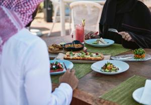 een groep mensen aan een tafel met borden eten bij Le Meridien Al Aqah Beach Resort in Al Aqah