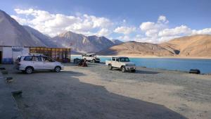 two cars parked next to a building next to a lake at Soma Retreat Cottage, Pangong Lake in Kakstet