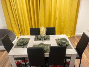 a dining room table with chairs and a yellow curtain at The Leckhampton - Company and Family Stays Chester Road in Walsall