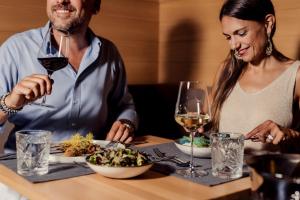 a man and woman sitting at a table with a plate of food and wine at Hotel SeeRose in Bodensdorf