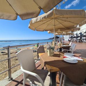 einen Tisch mit Stühlen und Sonnenschirmen am Strand in der Unterkunft Apartamento Playa Chica in Las Palmas de Gran Canaria