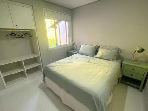 Schlafzimmer mit einem Bett mit weißer Bettwäsche und einem Fenster in der Unterkunft Apartamento 3 suítes Camburi in Camburi