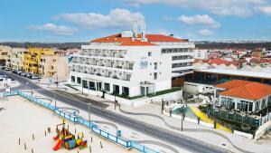 a large white building with a red roof on a city street at Hotel Cristal Vieira Praia & SPA in Praia da Vieira