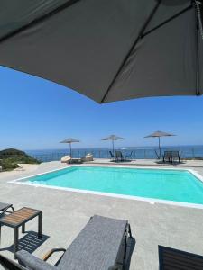 una piscina con sedie, ombrelloni e oceano di MELIKIRON LUXURY APARTMENTS a Ayios Nikitas