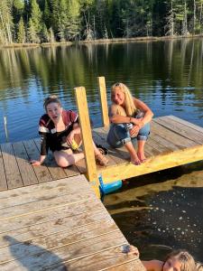 three girls sitting on a dock on a lake at Ladd Pond Cabins and Campground, LLC in Colebrook