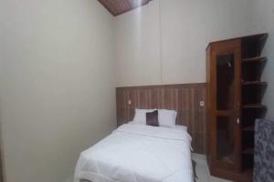 - une chambre avec un lit blanc et une tête de lit en bois dans l'établissement OYO 92628 Raja Alam Homestay, à Karanganyar