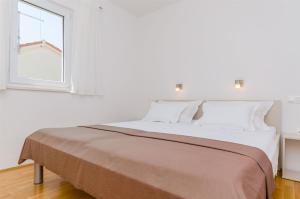 a white bedroom with a large bed with a window at Guesthouse Maestral in Trogir