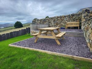 a wooden picnic table in front of a stone wall at Amazing coastal & sunset views in Eryri (Snowdonia) in Llanllyfni