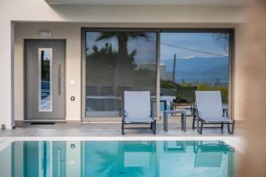 a house with a swimming pool and two chairs and a table at Jarko Luxury Houses in Argoulidhés