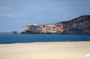 a beach with a cliff and the ocean with a person on it at Hotel Mare in Nazaré