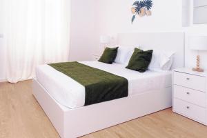 a white bedroom with a white bed with green pillows at Sunscape Nature Apt de 1 quarto Ponta do Sol in Ponta do Sol