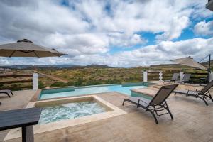 a swimming pool with chairs and an umbrella on a deck at Boskenvid Hotel - Romantic Treehouses & Skypool in Valle de Guadalupe