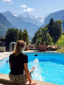 a woman sitting on a ledge by a swimming pool at Hotel Berghof Amaranth in Wilderswil