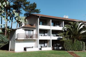 een groot wit gebouw met palmbomen en gras bij Hôtel Les Fougères in Hossegor