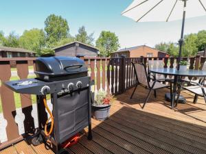 a grill on a deck with a table and an umbrella at Doormouse Lodge in Carnforth