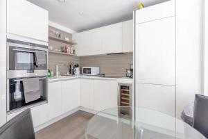 Modern 2BD Flat with a Balcony - Wandsworth في لندن: مطبخ مع دواليب بيضاء وطاولة زجاجية
