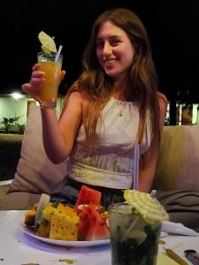 a woman holding a drink in front of a plate of food at French garden Pragash Beach Hotel in Trincomalee