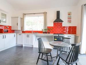 a kitchen with white cabinets and a table and chairs at 18 Ffordd Tanrallt in Prestatyn