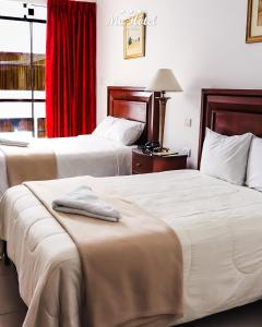 two beds in a hotel room with a red curtain at Mc Hotel Ica in Ica