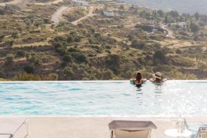 2 personnes dans une piscine avec une colline en arrière-plan dans l'établissement Noble 7 Suites - Adults Only - Onar Hotels Collection, à Parikia