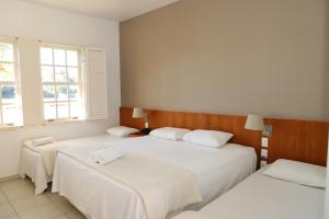 two beds in a room with white walls and windows at Engenho da Serra Hotel EcoResort in Capitólio