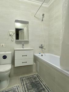 La salle de bains blanche est pourvue d'une baignoire, de toilettes et d'un lavabo. dans l'établissement Mangilik Cozy Apartment, à Astana