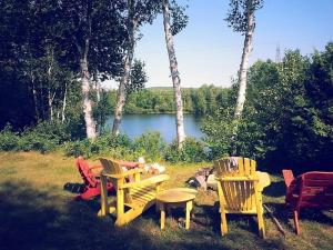 a group of chairs and tables in the grass near a lake at Le Chouette Chalet in La Malbaie