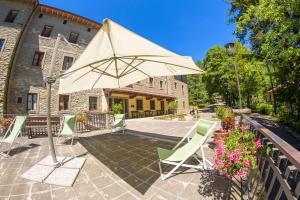 a patio with aige umbrella and green chairs at Casa PerFerie “PASTOR ANGELICUS” in La Verna