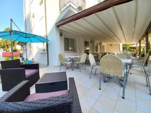 une terrasse avec des chaises, des tables et un parasol dans l'établissement Hotel Sasselli, à Cesenatico