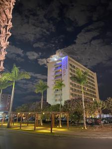 a tall building with palm trees in front of it at San Diego Suites Veredas Sete Lagoas in Sete Lagoas