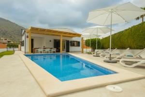 a pool with chairs and umbrellas next to a house at Alcudia Beach House in Alcudia