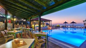 a restaurant with a large swimming pool with tables and chairs at Everest Apartments and Suites in Stalida