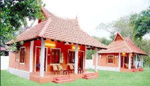 a small red house with a roof on the grass at Dazzle Dew in Alleppey
