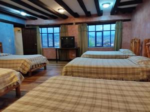 Habitación con 3 camas, TV y ventanas. en Hotel Achik Wasi, en Saraguro