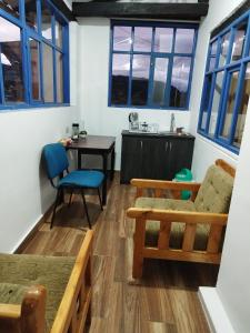 Hotel Achik Wasi في Saraguro: غرفة معيشة بنوافذ زرقاء وطاولة وكراسي