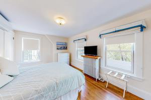 a bedroom with a bed and a tv and two windows at Bees Knees House in Boothbay Harbor