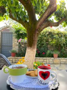 zwei Tassen Kaffee auf einem Tisch vor einem Baum in der Unterkunft Vjosa Guest House in Memaliaj