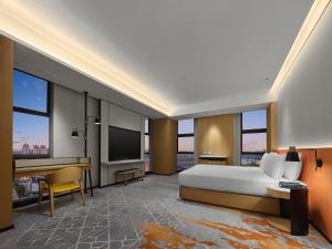 a bedroom with a bed and a desk with a television at Hilton Garden Inn Jiaxing Xiuzhou in Jiaxing