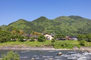 einen Fluss mit Häusern und Bergen im Hintergrund in der Unterkunft リバーサイドひの in Hino
