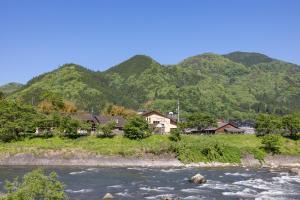 une rivière avec des maisons et des montagnes en arrière-plan dans l'établissement リバーサイドひの, à Hino