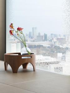a vase with flowers on a table in front of a window at HOTEL GROOVE SHINJUKU, A PARKROYAL Hotel in Tokyo