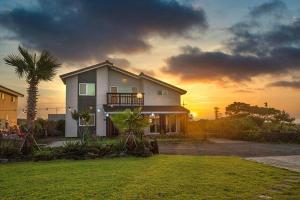 a house with a palm tree in front of a sunset at Arche House B in Jeju