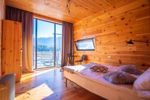 ein Schlafzimmer mit einer Holzwand mit einem Bett und einem großen Fenster in der Unterkunft Svaneti Сountryside 1 in Shkaleri