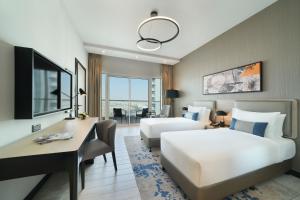 Habitación de hotel con 2 camas y escritorio en DAMAC Hills 2 Hotel, an Edge by Rotana Hotel, en Dubái