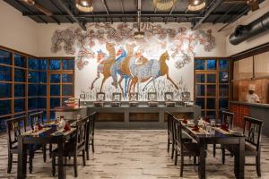 a restaurant with tables and chairs and a wall with a painting at Saj In The Forest, Pench National Park in Seonī