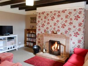 a living room with a fireplace and a red couch at Beech Cottage in Hepple